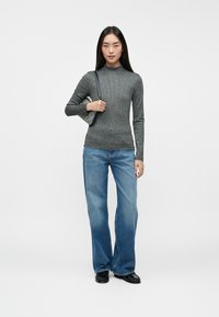 Grå ribbet langærmet top med høj hals, parret med lyseblå flagrende jeans og sorte sko, og holder en lille mønstret håndtaske.