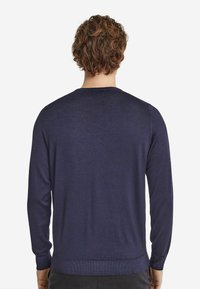 Mörkblå långärmad tröja med rund halsringning, slät textur, ribbade ärmslut och nederkant, som visar en figurnära bakdesign.