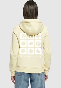 Felpa di un delicato giallo chiaro realizzata in morbido tessuto; presenta una grafica di nove motivi floreali e la scritta "Rinascita & Rinnovamento" sul retro.