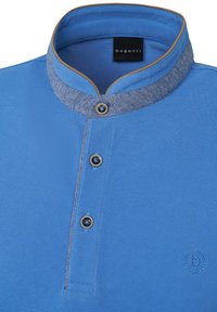 Blaues Poloshirt aus texturiertem Stoff, mit einem kontrastierenden Denim-Kragen und goldfarbenen Knöpfen. Gesticktes Logo an der Seite.