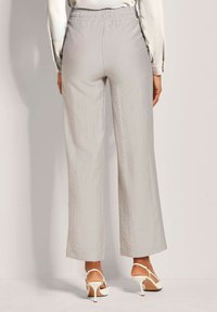 Lichtgrijze, wijde broek met een elastische tailleband. Gevoelige stof zichtbaar. Gepaard met witte hoge hakken.