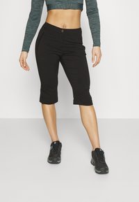 Black cropped pants feature a slim fit, zippered pockets, and a button closure. Worn with black athletic shoes.