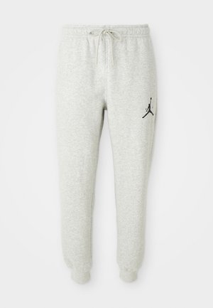 Pantalones deportivos gris claro con cintura elástica y cordón, tobillos con puños y un logo negro de Jordan en el muslo izquierdo.