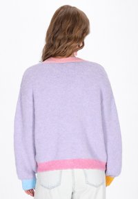Pulover pastel cu o textură pufoasă, având un corp lavandă, guler roz, mansete albastre și o croială lejeră. Mâneci lungi și largi.
