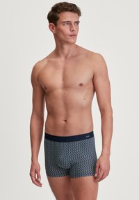 Men's blue boxer briefs with a zigzag pattern, made of soft fabric. Features a dark waistband with a logo and snug fit.