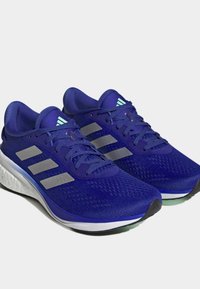 Purple running shoes with a mesh upper, three silver stripes, and a white midsole. Features textured fabric and rounded toe design.