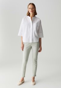 Camicia bianca con bottoni, colletto rotondo e maniche a tre quarti, abbinata a pantaloni fitted verde chiaro e scarpe beige senza lacci.