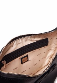 Borsa a mano nera in pelle con una texture liscia e hardware dorato. L'interno presenta un rivestimento beige con il logo "GUESS" ripetuto e una tasca con zip.