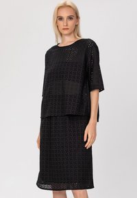 Ensemble noir en deux pièces comprenant un haut ample et une jupe. Le tissu présente un motif perforé avec des motifs floraux et une texture douce.