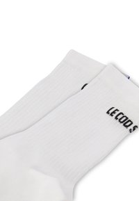 Calcetines de cuello blanco hechos de algodón, con textura acanalada y logo negro impreso en el lateral. Diseño sencillo, adecuado para uso casual.