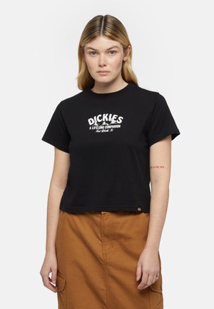 Maglietta nera corta con testo bianco che legge "DICKIES UN COMPAGNO PER LA VITA". Ha maniche corte e un orlo dritto. Sottostante una gonna marrone.