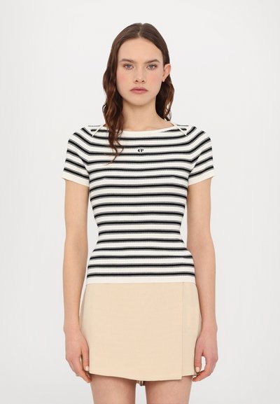 Top aderente a righe bianco e nero con maniche corte e scollatura rotonda, abbinato a una mini gonna beige. Dettagli in tessuto testurizzato visibili.