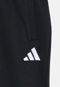 Black sweatpants made of textured fabric, featuring a white three-stripe logo on the left side near the pocket.