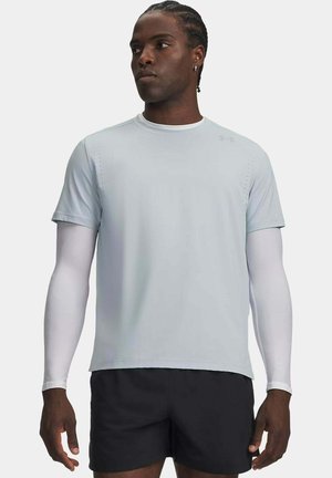Uomo che indossa una maglietta sportiva grigio chiaro a manica corta sopra maniche lunghe bianche e pantaloncini neri su uno sfondo uniforme.