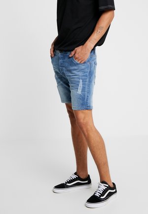 Shorts di jeans in azzurro con finitura consumata e leggero scolorimento. Abbinati a sneakers nere con dettagli bianchi. Design semplice.