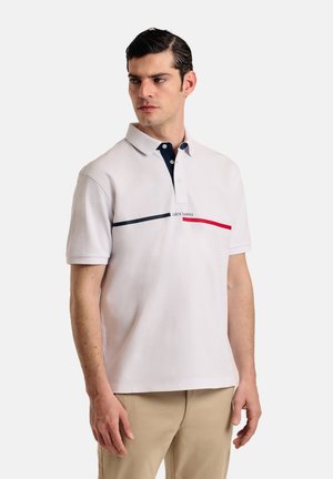 Camisa polo blanca con cuello marino, con rayas horizontales rojas y marinas, y un pequeño logo. Hecha de una tela suave, de mangas cortas.