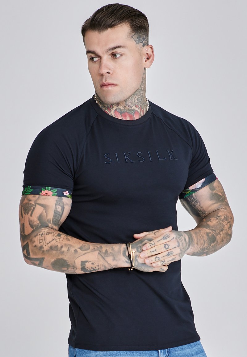 Marineblauwe T-shirt met korte mouwen en bloemenprint op de mouwen, aansluitend ontwerp en reliëf "SIKSILK" logo op de borst. Voorzien van een ronde hals en raglanmouwen.