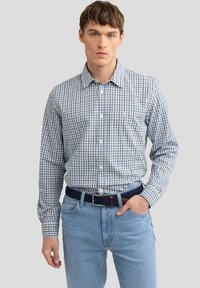 Gecarodeerde blouse in wit, marineblauw en lichtblauw, met een klassieke kraag en lange mouwen. Gecombineerd met lichtblauwe jeans en een geweven riem.