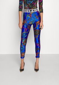 Leggings azules coloridos con intrincados patrones en rojo, verde y dorado, y una cinturilla de marca blanca. Diseño ajustado y textura brillante.