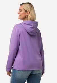 Felpa viola con tasca a marsupio, cappuccio foderato, polsini a coste e vestibilità casual. Abbinata a jeans azzurri chiari.