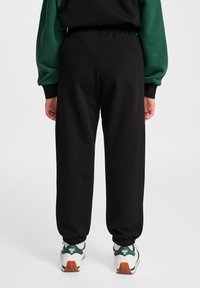 Czarne dresy z elastycznym pasem i rękawami, wykonane z miękkiego materiału. Noszone z białymi i zielonymi trampkami z teksturowaną podeszwą.