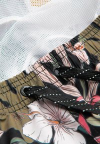 Gros plan sur un short de bain à motif floral avec des cordons noirs et une doublure en mesh blanche dessous.