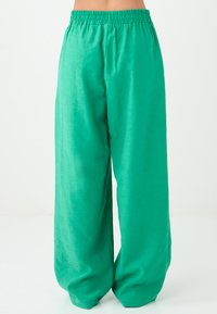 Groene brede broek gemaakt van lichtgewicht stof; heeft een elastische tailleband en een zachte, licht glanzende textuur.