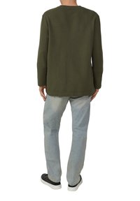 Olijfgroene blouse met lange mouwen en een ronde hals, gecombineerd met lichtblauwe rechte spijkerbroek en zwarte sneakers met witte zolen.