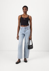 Top corto nero con logo rosa, jeans a gamba larga blu chiaro, scarpe nere flat e una piccola borsa nera con dettaglio del logo.
