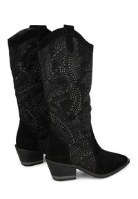 Botas de vaquero de ante negro con detalles texturizados en negro que presentan patrones geométricos. Punta ligeramente afilada y tacón bajo y apilado.