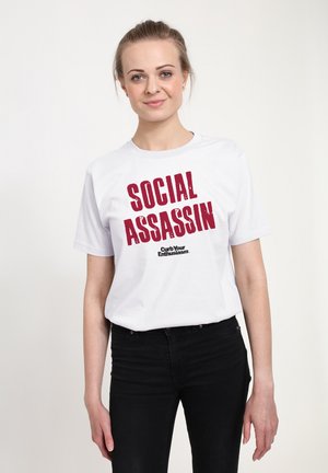 Maglietta bianca in cotone con una spiccata stampa grafica rossa che recita "SOCIAL ASSASSIN" e il logo di "Curb Your Enthusiasm" sottostante. Design fit.