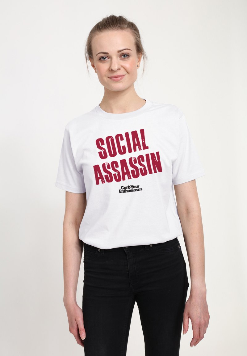 Bílý bavlněný tričko s výrazným červeným grafickým potiskem, který nese nápis "SOCIÁLNÍ ZABIJÁK" a logo "Curb Your Enthusiasm" pod ním. Střih přiléhavého typu.