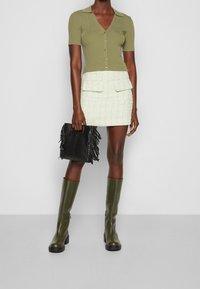 Oliwkowy prążkowany top z krótkim rękawem w serek, z złotymi guzikami, zestawiony z miętowym tweedowym mini spódnicą z dwiema kieszeniami. Czarna torebka z frędzlami.