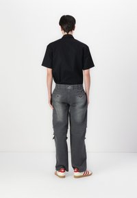 Black short-sleeve shirt paired with gray distressed wide-leg jeans and red-striped shoes. Notable detailing includes back pockets and frayed edges.