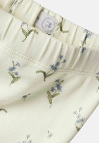 Ceinture florale en coton avec des motifs bleus et verts sur fond crème, élastique pour le stretch, avec une fermeture à bouton.