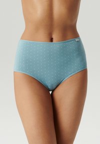 Kobieta nosząca jasnoniebieskie majtki o wysokim stanie z małymi białymi wzorami krzyży, przedstawiona od talii do górnej części ud na neutralnym tle.