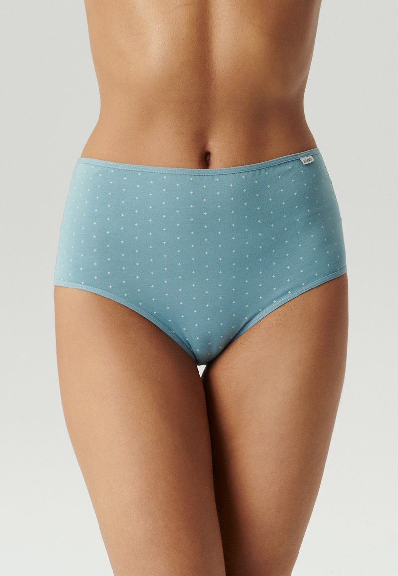 Kobieta nosząca jasnoniebieskie majtki o wysokim stanie z małymi białymi wzorami krzyży, przedstawiona od talii do górnej części ud na neutralnym tle.