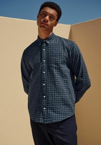 Lange mouw knoopshirt in donker marineblauw met een ruitpatroon. Bevat een kraag, borstzak en een gestructureerde stof.