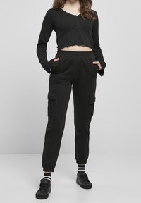 Svart kortärmad topp med knappar, och svarta cargo byxor med elastiska muddar och sidofickor, parat med svarta sneakers och randiga strumpor.