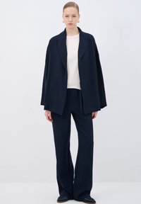 Navy blue loosely-fitted jacket with wide sleeves and a shawl collar, paired with matching wide-leg pants and a light-colored top beneath.