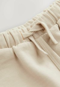 Tissu crème avec un tricot texturé, doté d'une taille ajustable et d'un cordon de serrage. Texture douce, détails de couture minimalistes.