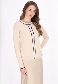 Beige lange mouw cardigan met marineblauwe stiksels en knopen. Heeft een ronde halslijn en een gemêleerde gebreide stof. Eenvoudig, casual ontwerp.
