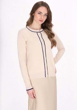 Beige lange mouw cardigan met marineblauwe stiksels en knopen. Heeft een ronde halslijn en een gemêleerde gebreide stof. Eenvoudig, casual ontwerp.