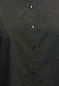 Camisa negra de botones, hecha de un tejido suave con un acabado nítido, que presenta botones de plástico negro en la parte delantera para el cierre.