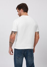 Hvid kortærmet T-shirt med rund hals, lavet af blødt stof. Minimalistisk design med en ensfarvet ryg. Bår med blå denimjeans.