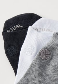 Tri para nogavic v črni, beli in sivi barvi. Izdelane so iz teksturiranega materiala z v krogu uvezenimi logotipi v ujemajočih se barvah na vsaki nogavici.