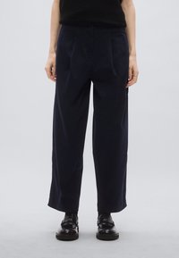 Marineblauwe wijde broek met plooien aan de voorkant, een knoopsluiting en een gladde textuur. Gecombineerd met zwarte schoenen voor een stijlvolle uitstraling.