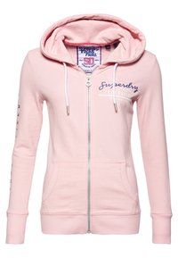 Sudadera rosa con cremallera hecha de algodón suave. Cuenta con una capucha, bolsillos frontales y texto impreso en el pecho y la manga en colores contrastantes.