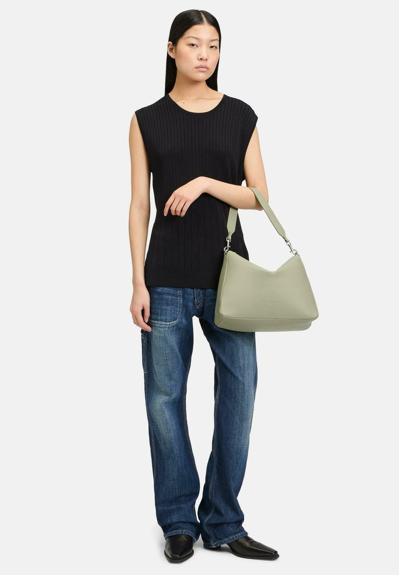 Grüne Lederhandtasche mit geschwungener Form und verstellbarem Riemen, kombiniert mit einem schwarzen gerippten Top und blauen weit geschnittenen Jeans.