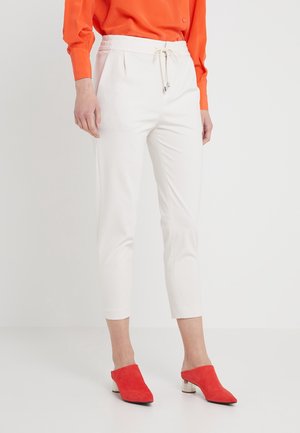 Femme porte un pantalon court blanc avec cordon, un chemisier orange vif à manches longues et des mules rouges à talon bas.